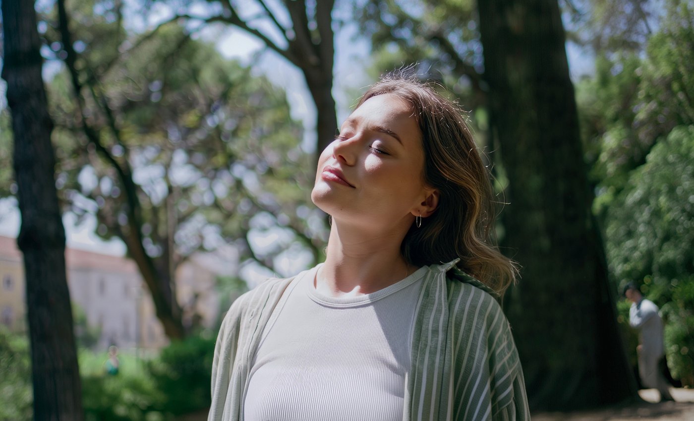 Mulher de olhos fechados respirando ao ar livre, entre árvores